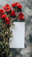 Vibrant red anemone flowers with green stems arranged alongside blank white card on textured grey background, creating elegant floral composition for wedding stationery.