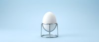 White egg in modern wire holder on clean blue background for kitchen design and cooking concepts.
