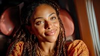 Young African American woman with braided hair smiling warmly while traveling in luxury airplane cabin during golden hour flight journey.