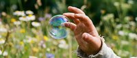 Hand reaching for a shimmering soap bubble in a blooming wildflower meadow, capturing a moment of wonder and childhood joy outdoors.