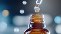 Liquid medicine drops falling into amber glass bottle with blurred bokeh background, close-up view showing pharmaceutical dosage preparation.