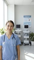 Smiling female healthcare professional in blue scrubs with stethoscope standing in modern medical office with equipment and natural light from windows.