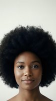 Young African American woman with natural afro hairstyle and glowing skin against neutral background for beauty and skincare campaigns.