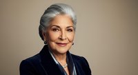 Senior woman with gray hair wearing dark blazer against neutral background, suitable for corporate, business, and professional website use.