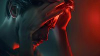 Man experiencing severe headache or migraine, holding head in pain with dramatic red and blue lighting, expressing stress and discomfort for healthcare and wellness concepts.