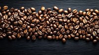 Fresh roasted coffee beans scattered in horizontal line on dark stone background, dramatic lighting highlights rich brown tones and natural texture.