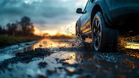 SUV driving through muddy puddle on rural road at sunset, creating dramatic splash against colorful evening sky.
