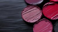 Colorful lipstick samples in various pink and red shades with creamy texture on dark wooden background for cosmetic and beauty industry applications.