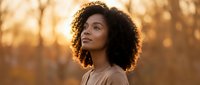Young African American woman with curly hair enjoying peaceful moment outdoors during golden hour sunset, natural beauty and wellness lifestyle concept.
