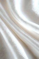Soft white silk fabric with gentle folds creating elegant waves and subtle texture, illuminated with natural light for luxurious wedding and fashion designs.