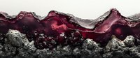 Red wine splashing against dark stones creates dramatic waves and bubbles, showcasing liquid motion in rich burgundy tones against textured rocky surface.