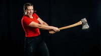 Strong athletic woman swinging sledgehammer with intense expression during workout training session on dark background for fitness motivation.
