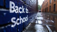 Back to school text on wet brick wall with blurred urban street background after rain, educational concept for autumn semester start and student return.