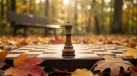 Wooden chess king piece standing on chessboard surrounded by colorful autumn leaves in park setting with golden sunlight and blurred trees background.