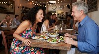 Mature couple enjoying romantic dinner date at cozy restaurant with wine and appetizers, laughing together in warm ambient lighting atmosphere.