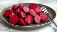 Sliced fresh beetroot on ceramic plate with fork, vibrant red vegetable pieces ready for healthy cooking or salad preparation.
