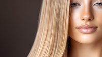 Young woman with straight blonde hair and natural makeup showing flawless glowing skin and full lips against brown background, beauty portrait closeup.