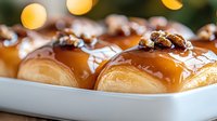 Fresh baked donuts topped with caramel glaze and candied pecans on white serving plate, extreme close up with selective focus and bokeh lights background.