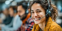 Smiling young woman with headset working in customer service call center, colleagues visible in background.