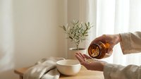 Hands pouring supplement capsules from amber bottle into palm, natural light interior, wooden table, wellness and healthy lifestyle concept.