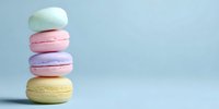 Stack of colorful macarons in pastel colors - mint, pink, lavender, and yellow - against light blue background with copy space.