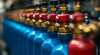 Row of industrial gas cylinders in red and blue with brass valves, shallow depth of field creates dramatic perspective in workshop environment.
