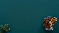 Cinnamon sticks and star anise spices arranged in glass bowl on teal background with evergreen branch and ornament for holiday cooking and seasonal culinary projects.