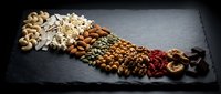 Assorted nuts and dried fruits arranged on dark slate board creating healthy snacking display for nutrition and wellness concepts.