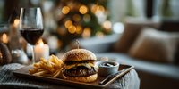 Gourmet burger with fries on wooden tray in cozy restaurant setting with wine glass and candlelight creating warm atmospheric dining experience.