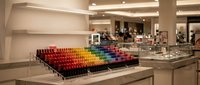 Professional cosmetics store interior with colorful lipstick display arranged in rainbow gradient on modern white counter in luxury retail space.