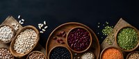 Assorted legumes and grains in wooden bowls on dark background. Healthy protein sources including beans, lentils, chickpeas for cooking and nutrition.