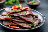Spicy marinated beef jerky slices garnished with fresh chili peppers and herbs on plate, protein snack ready for packaging and marketing materials.