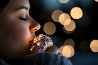 Young woman biting decorated donut with sprinkles against blurred bokeh lights background, side profile view creating dreamy atmospheric mood for food photography.