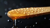 Honey dripping from wooden spoon with water droplets against dark background, macro food photography showing golden syrup texture and viscosity.