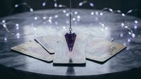 Mystical purple crystal pendulum suspended over tarot cards with glowing fairy lights creating magical atmosphere for divination and spiritual guidance sessions.