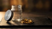 Empty glass jar with black lid and golden capsules spilled on rustic wooden surface. Warm lighting creates cozy atmosphere for supplement storage concept.