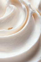Smooth swirls of creamy white meringue or whipped cream texture creating soft waves and curves, macro photography showing delicate details and light beige tones.