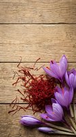 Saffron spice threads with purple crocus flowers on rustic wooden background for culinary and cooking applications.