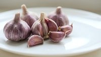 Whole and split garlic cloves with papery skin arranged on white plate for cooking, food preparation, culinary ingredients.