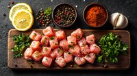 Raw diced tuna with spices, lemon, garlic and fresh herbs on wooden cutting board against dark background. Fresh ingredients for Asian cuisine preparation.