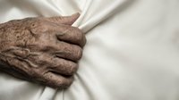 Senior person's wrinkled hand resting on white fabric, conveying aging, care, comfort, and tenderness for healthcare, wellness, and family concepts.