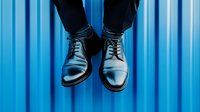 Elegant black leather oxford shoes floating against vibrant blue background. Minimalist business fashion concept with dramatic lighting and symmetrical composition.