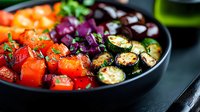 Colorful roasted vegetables in black ceramic bowl featuring red tomatoes, grilled zucchini and purple onions garnished with fresh herbs on dark background.