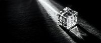 Crystal clear glass cube casting dramatic shadows on dark textured surface with bright light beam creating geometric patterns and reflections.
