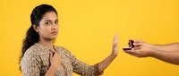 Young South Asian woman refusing cigarette offer with stop hand gesture against bright yellow background promoting healthy lifestyle choices and smoking cessation.