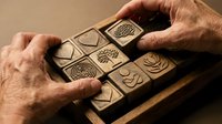 Artisan hands crafting wooden stamps with intricate nature patterns including trees, leaves and geometric designs for printmaking and creative projects.