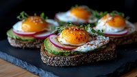 Open-faced sandwich with sunny side up egg, avocado, radish slices and microgreens on dark seeded bread, served on black slate board. Gourmet breakfast.