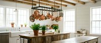 Rustic farmhouse kitchen interior with wooden island, copper pots hanging from rack, white cabinets, exposed beams and large windows for home design.