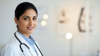 Professional female doctor with stethoscope smiling confidently in modern medical clinic environment for healthcare and wellness concepts.