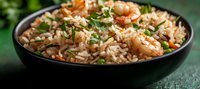 Savory shrimp fried rice garnished with fresh herbs in black bowl, mixed with colorful vegetables and tender seafood pieces on dark background.